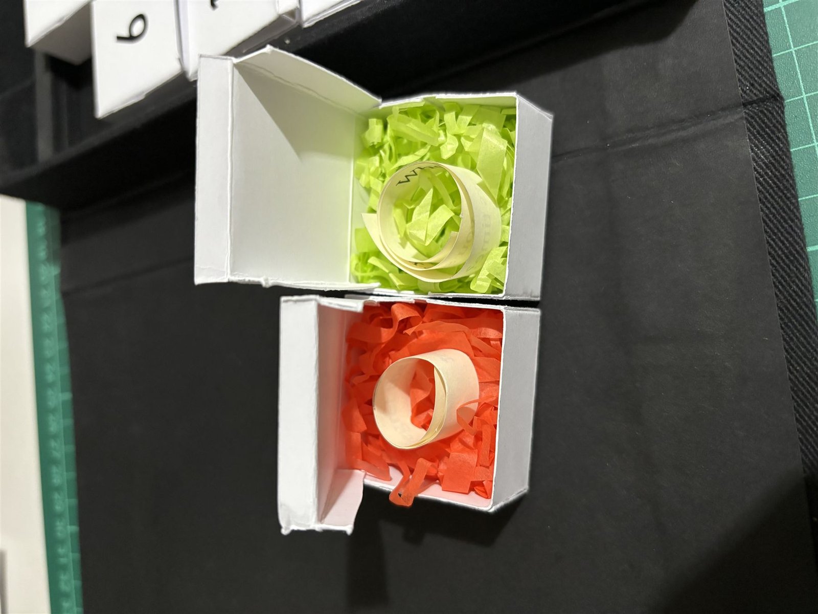 Two opened miniature boxes showing coloured tissue paper and rolled notes inside